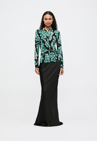 Blusa de mangas longas com padrão floral em verde e preto, combinada com uma saia ajustada em preto de satin, criando uma silhueta elegante.