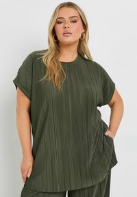 Olivgrön, plisserad oversized topp med korta ärmar, rund halsringning och avslappnat snitt. Har en subtil textur och sidficka.