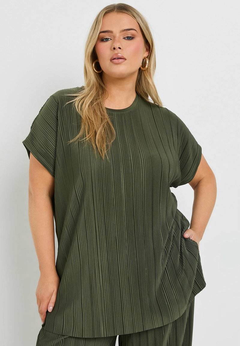 Olivgrön, plisserad oversized topp med korta ärmar, rund halsringning och avslappnat snitt. Har en subtil textur och sidficka.