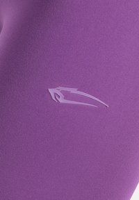 Lila träningsleggings gjorda av elastiskt tyg med en texturerad yta och en liten präglad logotyp på nedre högra sidan.