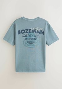 Hellblaues T-Shirt mit kurzen Ärmeln und dem Text "Bozeman Montana MT 59847" sowie kleineren Sprüchen, die Rückgrat und Service auf der Rückseite fördern.
