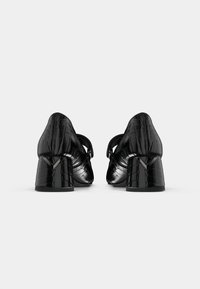 Chaussures à talon bloc en cuir synthétique noir effet crocodile, avec un design structuré et une texture détaillée, comprenant une lanière arrière et un accent de talon anglé.
