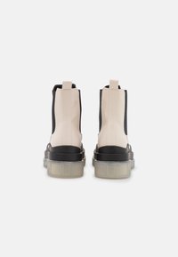 Chunky ankle boots featuring a beige and black design, smooth leather-like material, elastic side panels, and a transparent thick sole.
