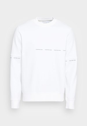 Weißes Sweatshirt mit langen Ärmeln und Rundhalsausschnitt, mit dünnen horizontalen schwarzen "Calvin Klein Jeans"-Schriftzügen über der Brust und an den Ärmeln.