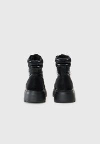 Botas negras de tobillo con un diseño acolchado, forro suave, lengüetas de tira y una suela de goma texturizada. Acabado liso y mate en toda la bota.