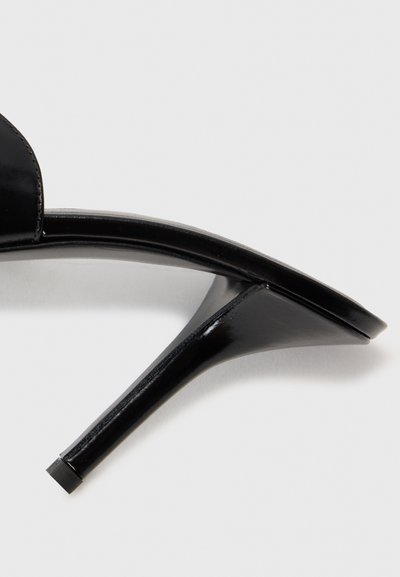 Sandale à talons hauts noire avec une finition brillante, design ouvert au niveau des orteils, talon stiletto fin et détails de bretelles minimalistes.