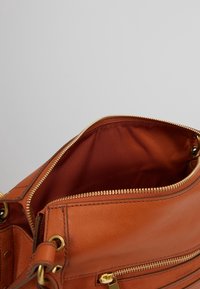 Brun lædertaske med lynlås, der har en glat overflade, guldfarvet hardware og en kontrasterende indvendig foring.