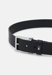 Cintura in pelle nera con una fibbia in metallo argentato, dotata di diversi fori per la regolazione e un accento con logo rosso, bianco e blu sul passamano.