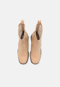 Tan ankle boots with a smooth, matte texture, featuring a side zipper and a contrasting black sole. Folded top with pull tab detail.
