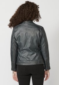 Giacca in pelle nera aderente con una finitura liscia, caratterizzata da un colletto semplice, polsini con zip e cuciture elaborate lungo la schiena.
