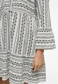 Robe à motifs noir et blanc avec des designs géométriques, des manches évasées et une jupe à volants en coton texturé.