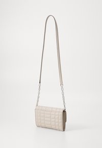 Crossbody-Tasche aus weichem, beigem, ge quiltetem Material, rechteckige Form, mit einem dünnen Schultergurt und Kettenakzenten.