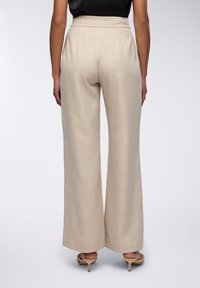 Pantaloni larghi beige realizzati in tessuto morbido, con vita alta e pieghe sottili, abbinati a tacchi di colore chiaro.