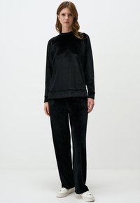 Ensemble de détente en velours noir avec manches longues et coupe décontractée, présentant un léger éclat. Le pantalon est large et assorti au haut.