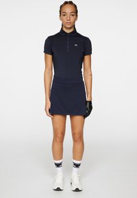 Robe polo bleu marine en tissu extensible, dotée d'un col, de manches courtes et d'une taille ajustée. Des gants noirs et des chaussettes blanches à motifs viennent compléter le look.