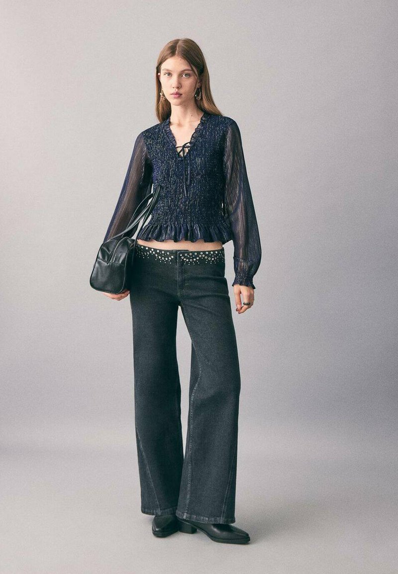 Mornarsko rebrasto bluzo s naborkom, sprednji del s vezanjem; črne visoko pasne flare kavbojke z srebrnimi bleščečimi detajli; črna torbica; gležnjarji.