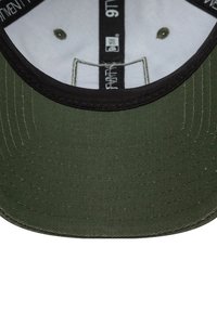 Zielona czapka z czarnym daszkiem, wykonana z teksturowanej tkaniny. Wewnątrz ma białą podszewkę i detale szwowe. Posiada metki z rozmiarem i marką.