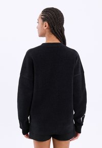 Μαύρη υπερμεγέθη μπλούζα με υφή, μακριά μανίκια και στρογγυλή λαιμόκοψη. Περιλαμβάνει μια διακριτική σχεδιαστική λεπτομέρεια στο μανίκι.