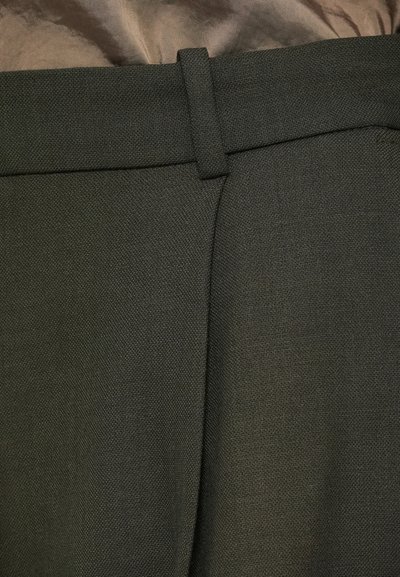 Pantaloni verzi închisi, cu un material texturat, design cu fața plată și bucle pentru centură la talie. Finisaj croițat, fără detalii de cusătură vizibile.