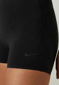 Crne rastezljive atletske kratke hlače glatke teksture, s diskretnim sivim Nike logom na donjoj lijevoj strani i ravnim šavovima.