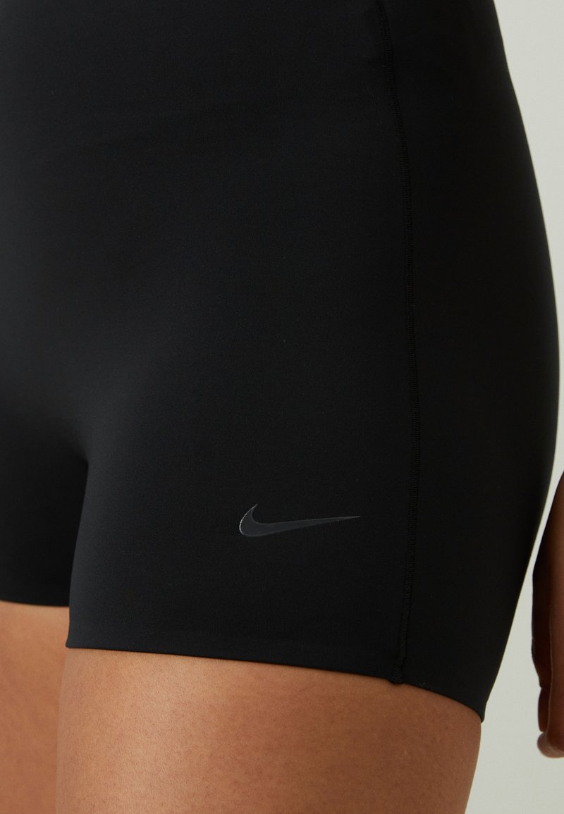 Pantalones cortos deportivos elásticos negros con una textura suave, que cuentan con un sutil logo de Nike en gris en la parte inferior izquierda y costuras planas.