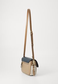 Crossbody bag in tan, cream, and navy leather with a top flap, adjustable strap, and gold hardware. Features a zippered pocket on the back.