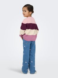 Pull tricoté avec des rayures horizontales en rose, prune et crème ; associé à un jean bleu clair orné de motifs de cœurs roses.