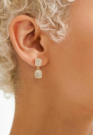 Kullatooni ripatsiga kõrvarõngad, mis koosnevad kahest ruudukujulisest osast, millest üks on kaetud mitmete väikeste läbipaistvate kivikestega ja millel on tekstuuriga pind.