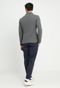 Blazer gris avec une coupe ajustée, présentant une texture lisse et un design structuré. Associé à des chinos bleu marine et des baskets blanches.