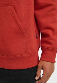 Red sweatshirt with a kangaroo pocket, ribbed cuffs, and hem. Cotton blend fabric with a smooth texture and subtle stitching details.
