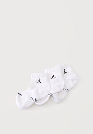 Trzy pary białych skarpetek za kostkę z czarnymi logo Jumpman i tekstem na mankietach, ułożonych obok siebie na jasnej powierzchni.