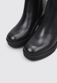 Bottines en cuir noir à bout rond, finition texturée, et semelle en caoutchouc noir épaisse ; dispose d'une fermeture éclair sur le côté pour un enfilage facile.
