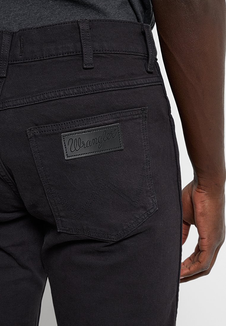 Czarne dżinsy mają zaokrągloną tylną kieszeń z czarną skórzaną metką Wrangler. Materiał ma subtelną teksturę.