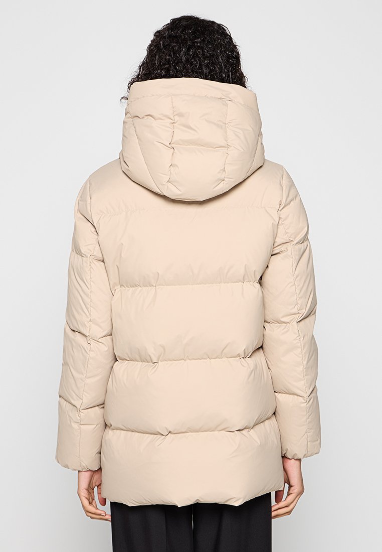 Beżowa kurtka puchowa z kapturem. Posiada pikowany design i lekko luźny krój. Materiał wydaje się gładki z minimalnym połyskiem.