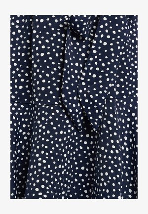 Navy dress with white polka dots, featuring a smooth fabric texture, a bow detail at the neck, and a flared skirt design.