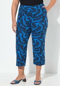 Pantalons courts bleus avec un motif de feuilles noires, dotés d'une taille élastique et de poches latérales, associés à des sandales à talons bleues.