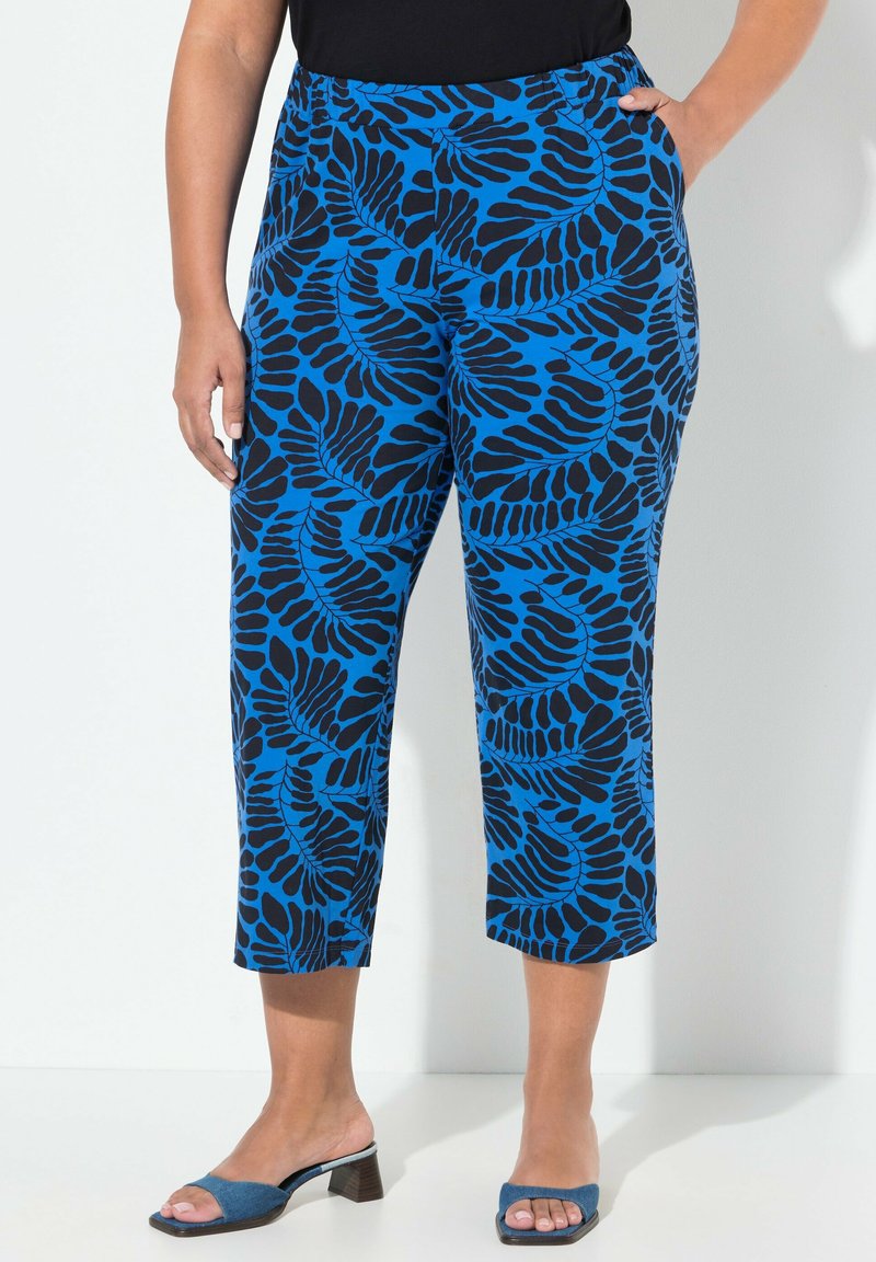 Pantalons courts bleus avec un motif de feuilles noires, dotés d'une taille élastique et de poches latérales, associés à des sandales à talons bleues.
