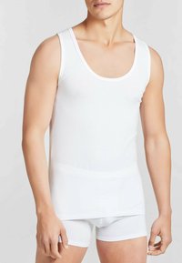 Top in cotone bianco senza maniche con scollatura a barca, design aderente e forma slim. Texture liscia e stile essenziale.