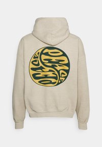 Sudadera con capucha de tela beige que presenta un gran gráfico circular en verde y amarillo con letras abstractas en la parte posterior.
