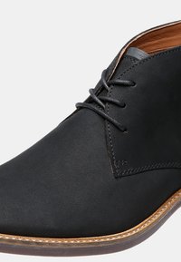 Chaussure habillée en cuir noir avec bout rond, lacets noirs, coutures marron et semelle marron avec des détails de couture visibles.