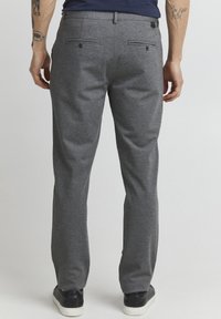 Gray tailored trousers showcasing a textured fabric, two back pockets with buttons, and a straight-leg cut, paired with dark sneakers.