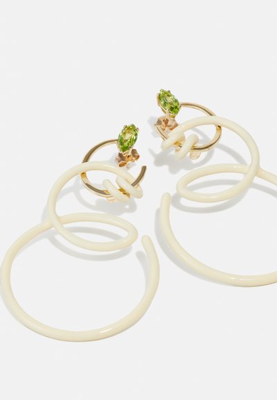 Pendientes de aro en forma de espiral de color blanco, con una textura suave, adornados con acentos de piedra verde sobre un hardware en tono dorado.