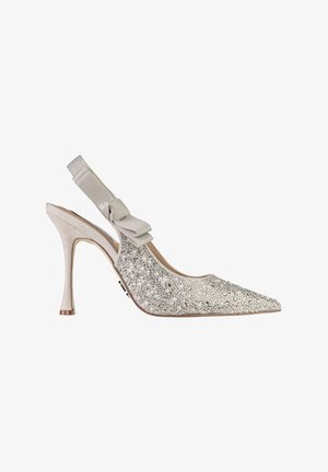 Scarpa beige con tacco alto e cinturino sul tallone, punta appuntita, decorata con perle e strass, e fiocco di stoffa sul cinturino.