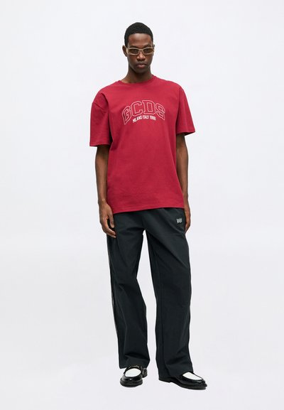 Crvena pamučna majica kratkih rukava s natpisom "GCDS MILANO ITALY 1988" u kontrastnoj bijeloj boji. U paru s crnim, širokim hlačama.