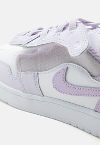 Λευκό και ανοιχτό μοβ αθλητικό παπούτσι Nike από την πλευρά με κορδόνια, πλέγμα, ραμμένα επικαλύμματα και λαστιχένια σόλα σε απλό φόντο.