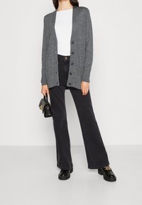 Szary, dziany kardigan z guzikami, noszony na białej bluzce, w połączeniu z czarnymi spodniami o szerokich nogawkach i czarnymi butami na platformie. Do kompletu czarna torebka.