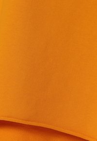 Kirkkaan oranssi kangas, jossa on sileä tekstuuri ja kevyt kiilto. Reunat on viimeistelty siististi, mikä korostaa materiaalin laatua.