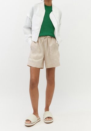 Veste bomber blanche légère, pull en maille verte, shorts en lin beige avec cordon de serrage, et sandales à enfiler crème avec une semelle épaisse.