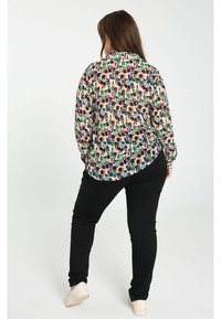 Blouse à manches longues avec un motif multicolore et un tissu lisse, associée à un pantalon noir ajusté. La blouse présente un ourlet courbé et une coupe décontractée.
