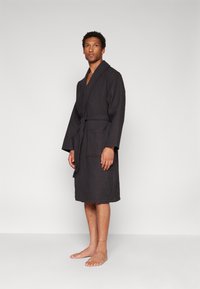 Black, textured bathrobe with long sleeves, waist tie, and front pockets, knee-length, featuring a woven pattern and solid color.